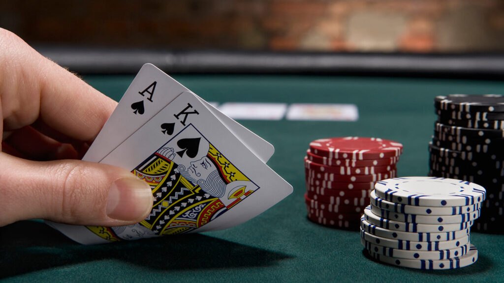 Mão com duas cartas em uma mesa de blackjack segurando as cartas de rei e às, mostrando parte do que é o blackjack